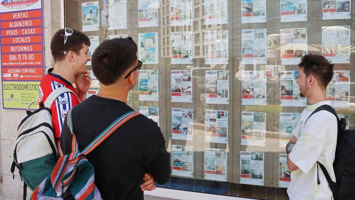 Jóvenes consultan anuncios de pisos en una inmobiliaria para independizarse en Galicia