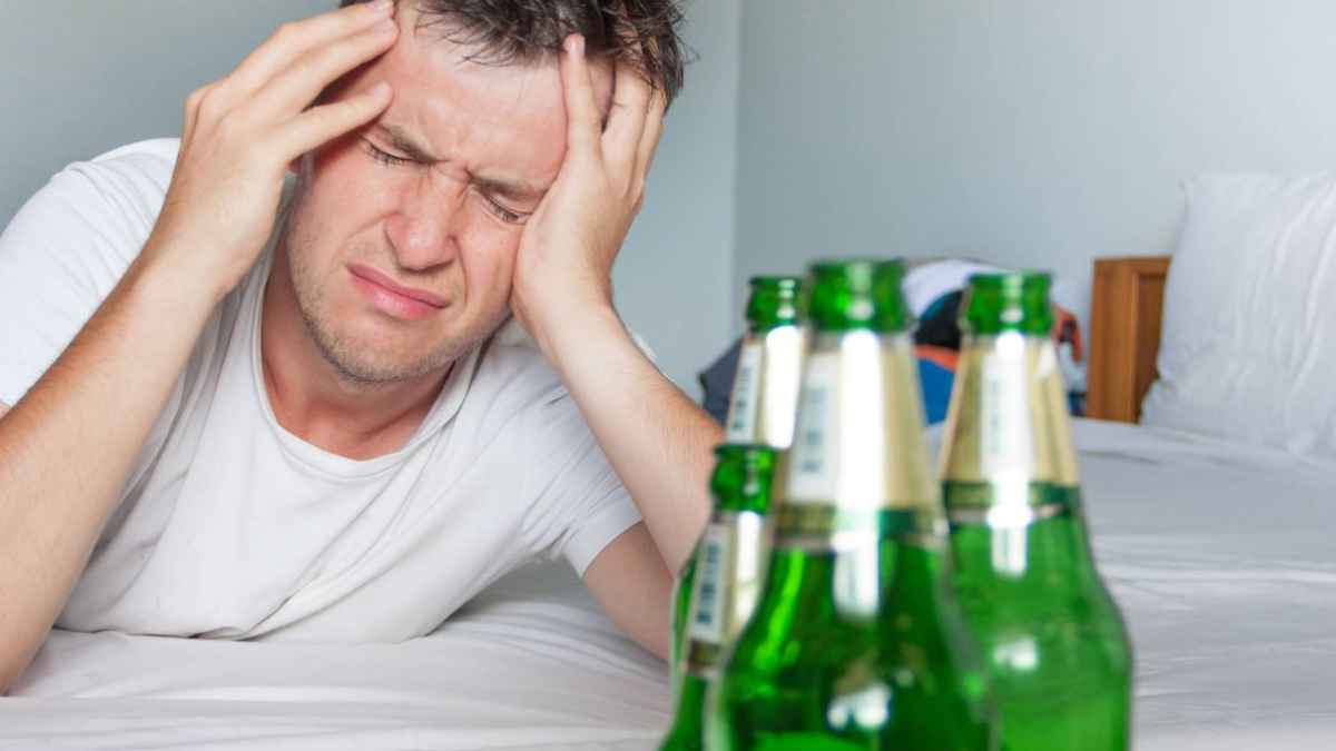 Hombre con fuerte resaca y dolor de cabeza junto a botellas de alcohol, una situación que en Alemania puede justificar faltar al trabajo
