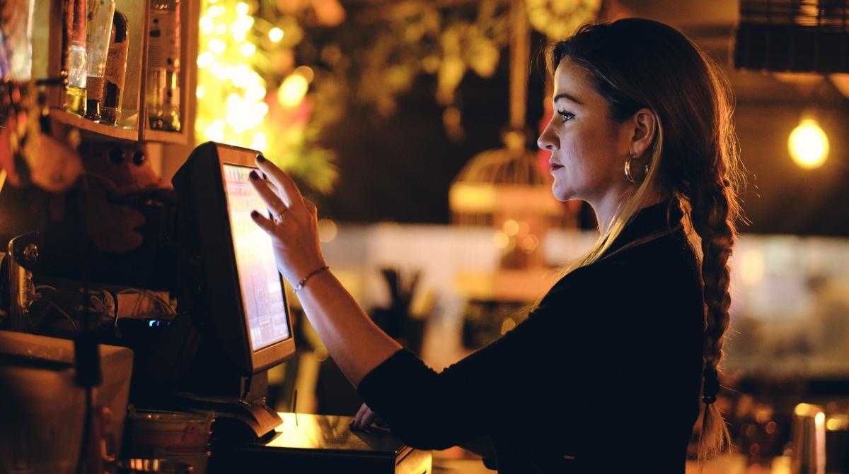 Camarera trabajando de noche en un bar usando TPV durante horario nocturno en España