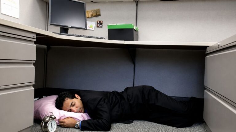 Trabajador durmiendo una microsiesta bajo su escritorio durante la jornada laboral para reducir el estrés y mejorar el rendimiento