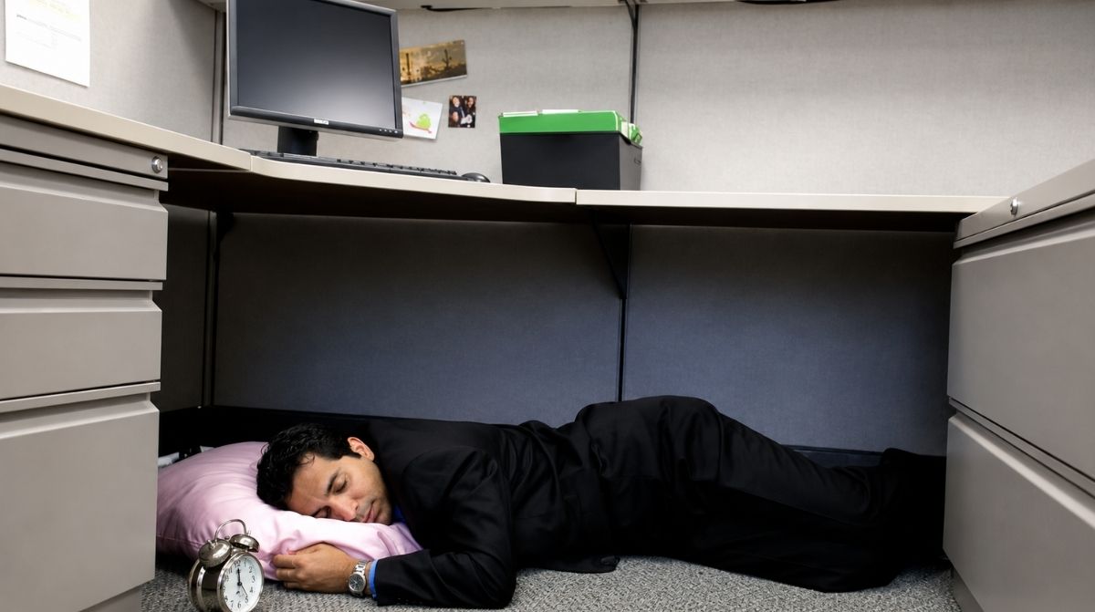 Trabajador durmiendo una microsiesta bajo su escritorio durante la jornada laboral para reducir el estrés y mejorar el rendimiento