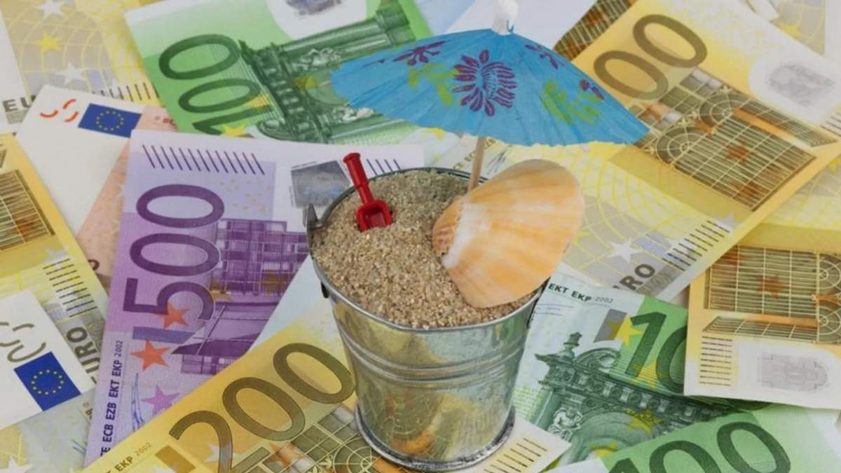 Paga extra de verano representada con billetes de euro y elementos de vacaciones sobre arena de playa