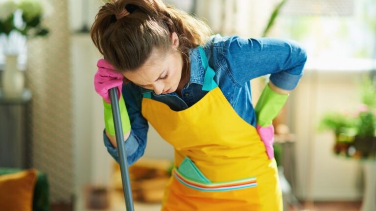Empleada del hogar con dolor de espalda mientras realiza tareas de limpieza tras la nueva formación del SEPE en prevención de riesgos laborales