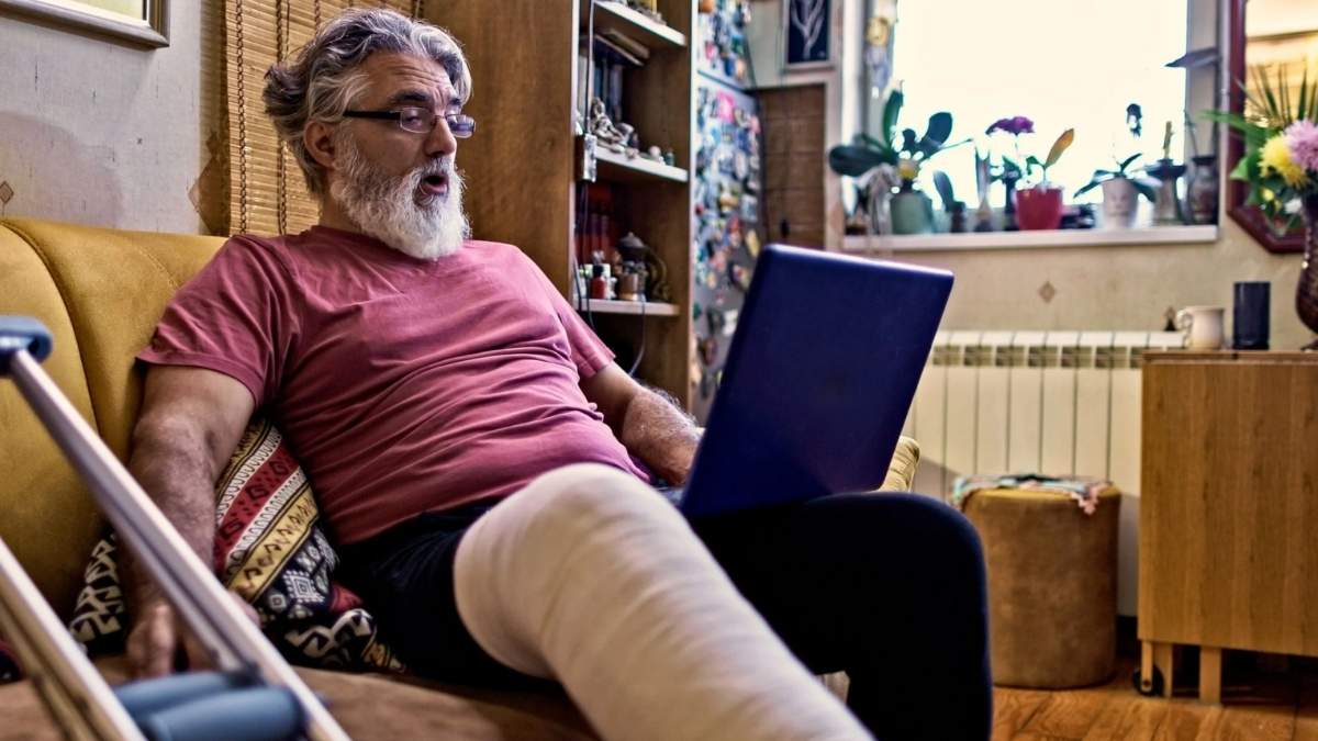 Trabajador de baja médica con la pierna escayolada usando un portátil desde casa durante su periodo de recuperación