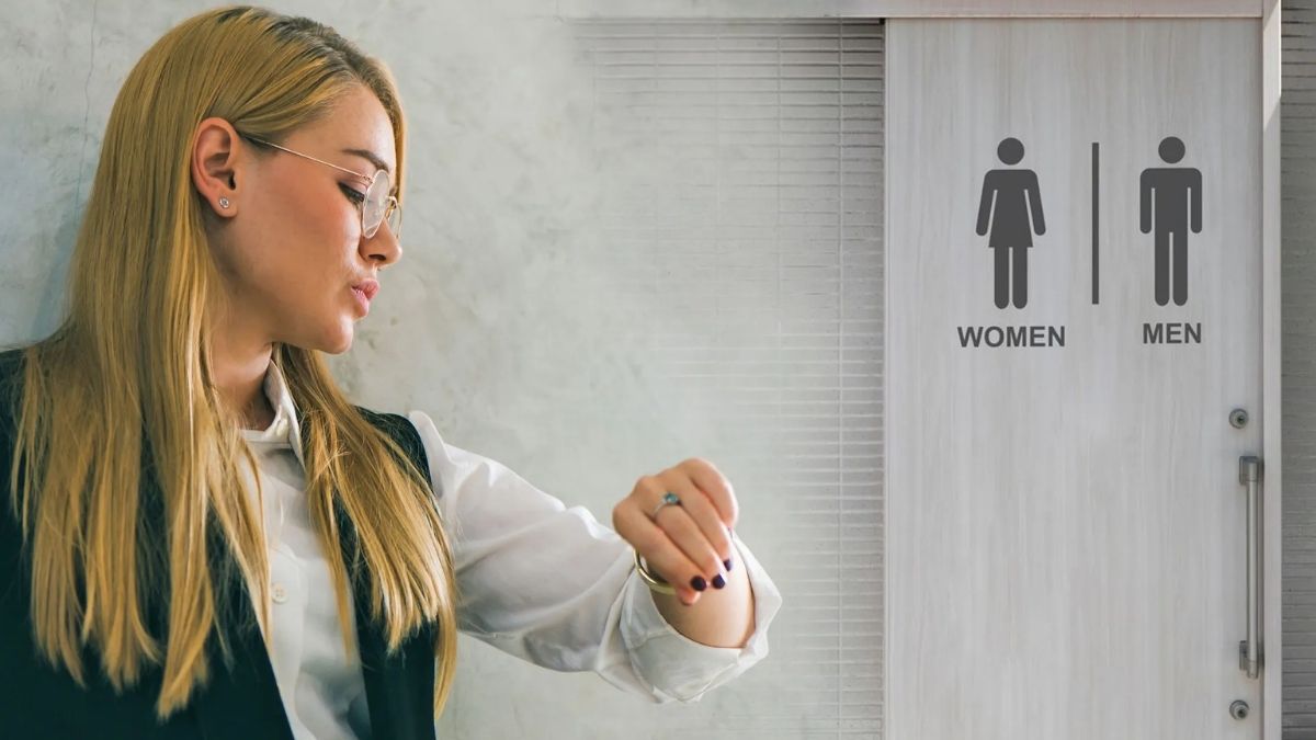 Trabajadora mirando el reloj frente a un baño en una oficina tras un caso de despido por largas pausas laborales