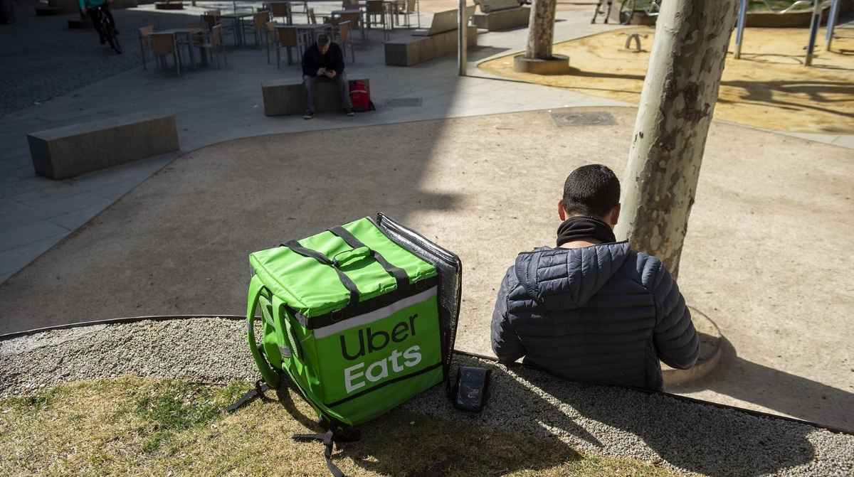 Trabajador de Uber Eats sentado junto a una mochila de reparto tras un despido declarado improcedente por la justicia