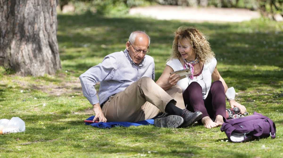 Pensionistas consultando el móvil en un parque durante el verano tras el cobro de la paga extra de la Seguridad Social