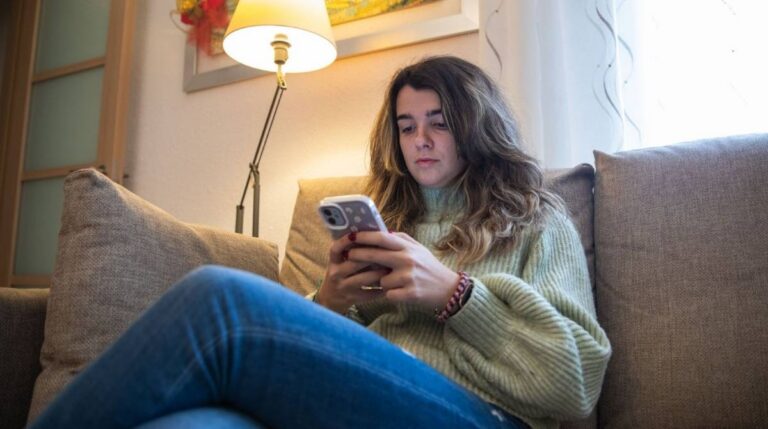 Mujer joven consultando el móvil desde el sofá para informarse sobre el Ingreso Mínimo Vital de la Seguridad Social