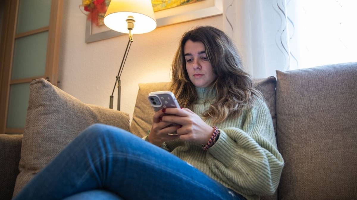 Mujer joven consultando el móvil desde el sofá para informarse sobre el Ingreso Mínimo Vital de la Seguridad Social