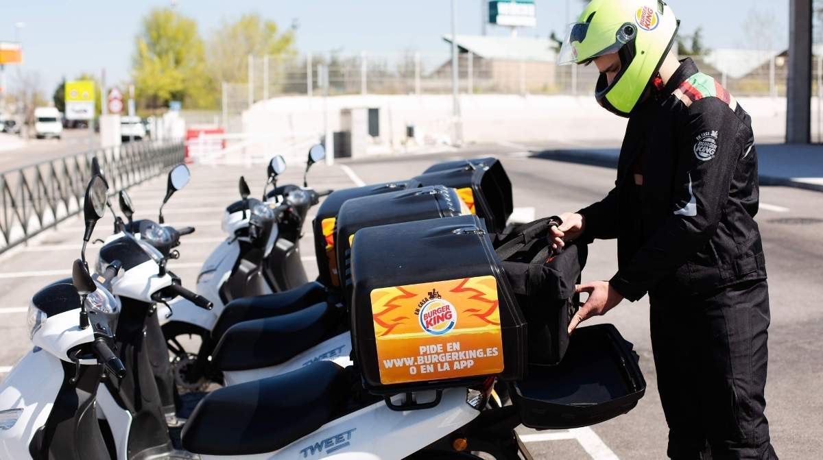 Repartidor de Burger King preparando un pedido junto a varias motos de reparto con uniforme de seguridad