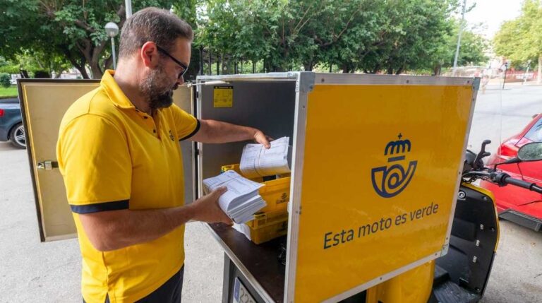 Cartero de Correos preparando envíos para reparto en una moto eléctrica durante la campaña de contratación de verano