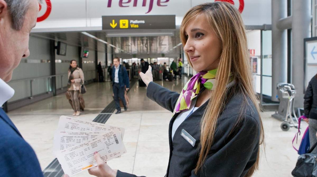 Trabajadora de Renfe atendiendo a un cliente en estación con billete en mano empleo sin oposicion