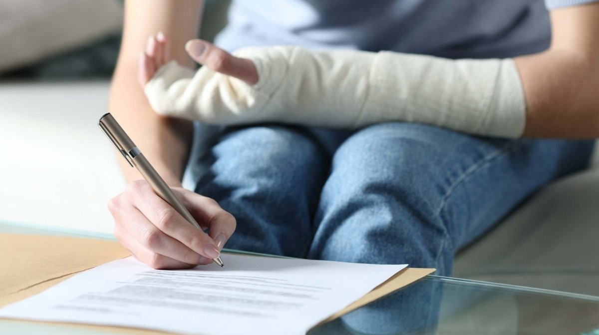 Trabajador con brazo escayolado firmando documento durante baja médica posible despido laboral