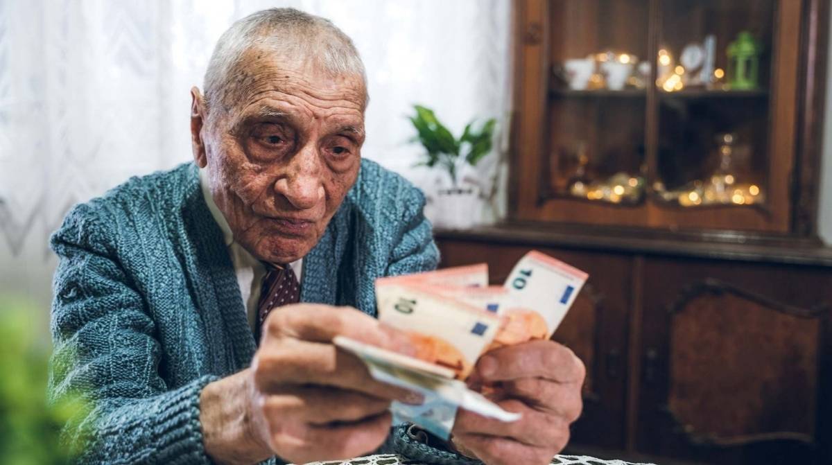 Persona mayor contando billetes de euro en su vivienda mientras revisa sus gastos económicos