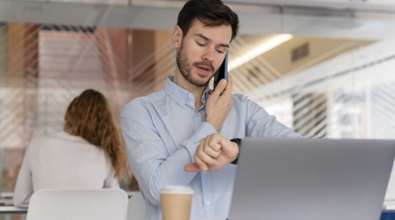 Trabajador revisando la hora mientras continúa trabajando después de su jornada laboral en una oficina