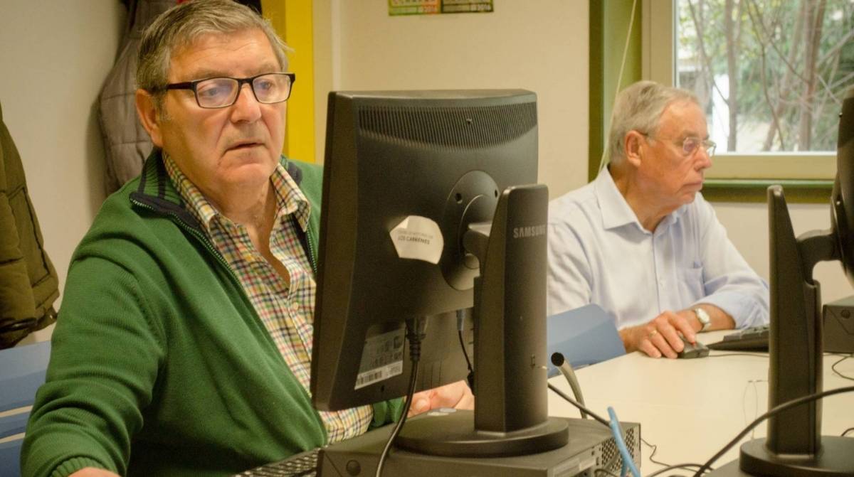 Dos personas mayores utilizan un ordenador en una oficina relacionado con el subsidio para mayores de 52 años.