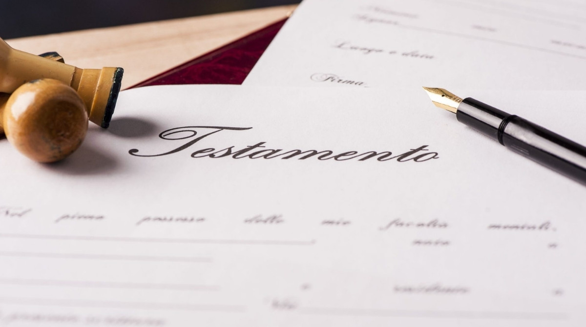 Testamento junto a un sello notarial y una pluma sobre un documento de herencia