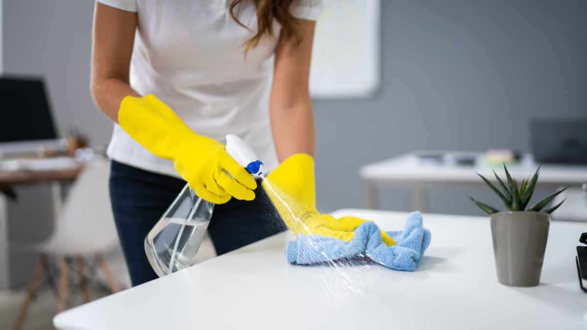 Mujer limpiando una mesa con guantes amarillos y productos de limpieza