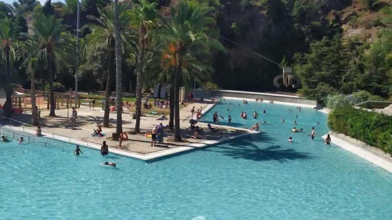Vista del lago artificial de Can Dragó, la piscina pública más grande de Barcelona, con zonas de baño, palmeras y amplios espacios verdes.