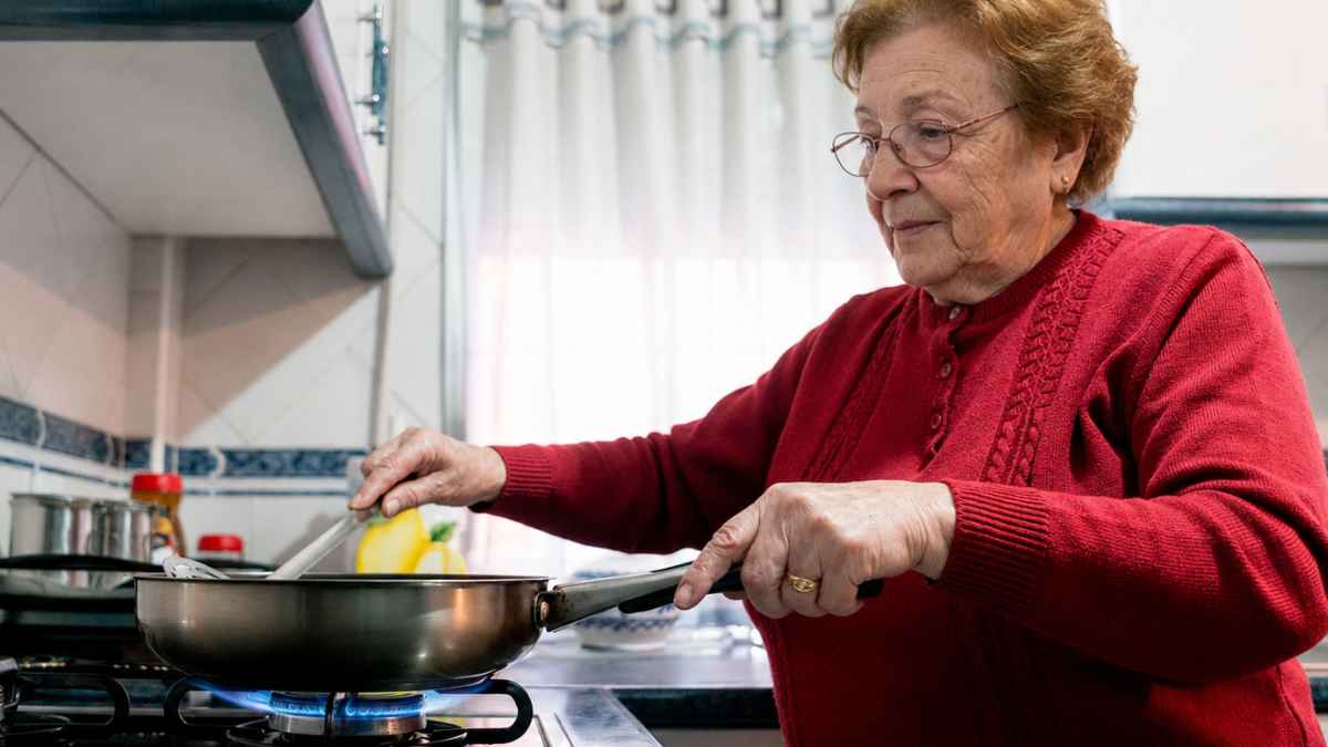 Mujer mayor cocinando en una vivienda familiar tras reclamar una compensación por las tareas del hogar