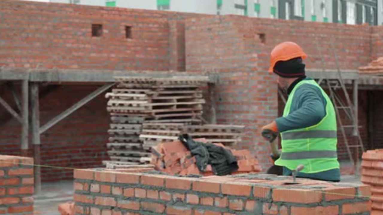 Albañil construyendo un muro de ladrillos en una obra mientras trabaja con casco y chaleco de seguridad.