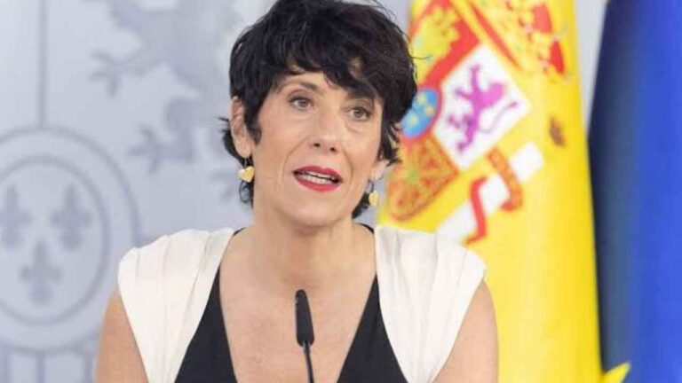 Mujer compareciendo ante los medios junto a una bandera de España por las ayudas para mayores de 52 años
