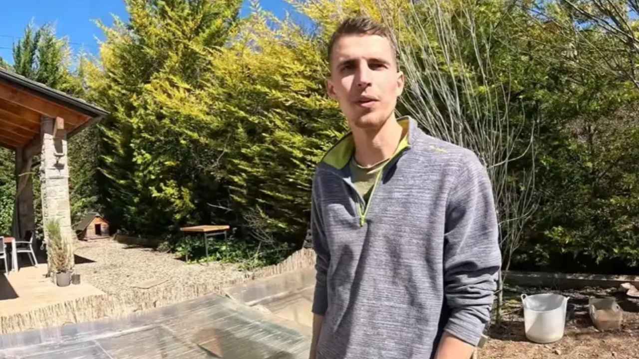 Arnau sostiene unas astas frente a una vivienda rural de piedra y madera.
