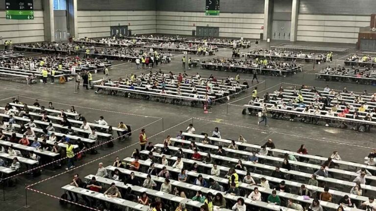 Aspirantes realizando un examen de oposiciones en un recinto con numerosas mesas