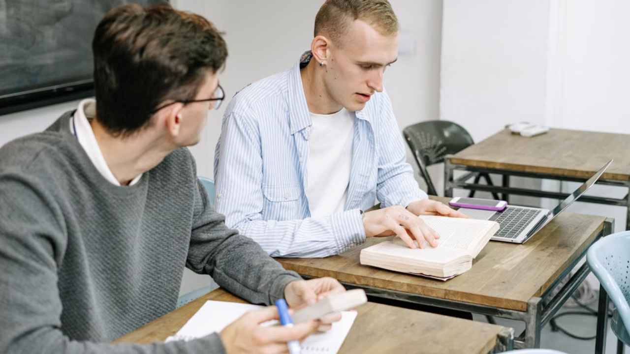Dos estudiantes trabajan con un ordenador portátil y libros en un aula.