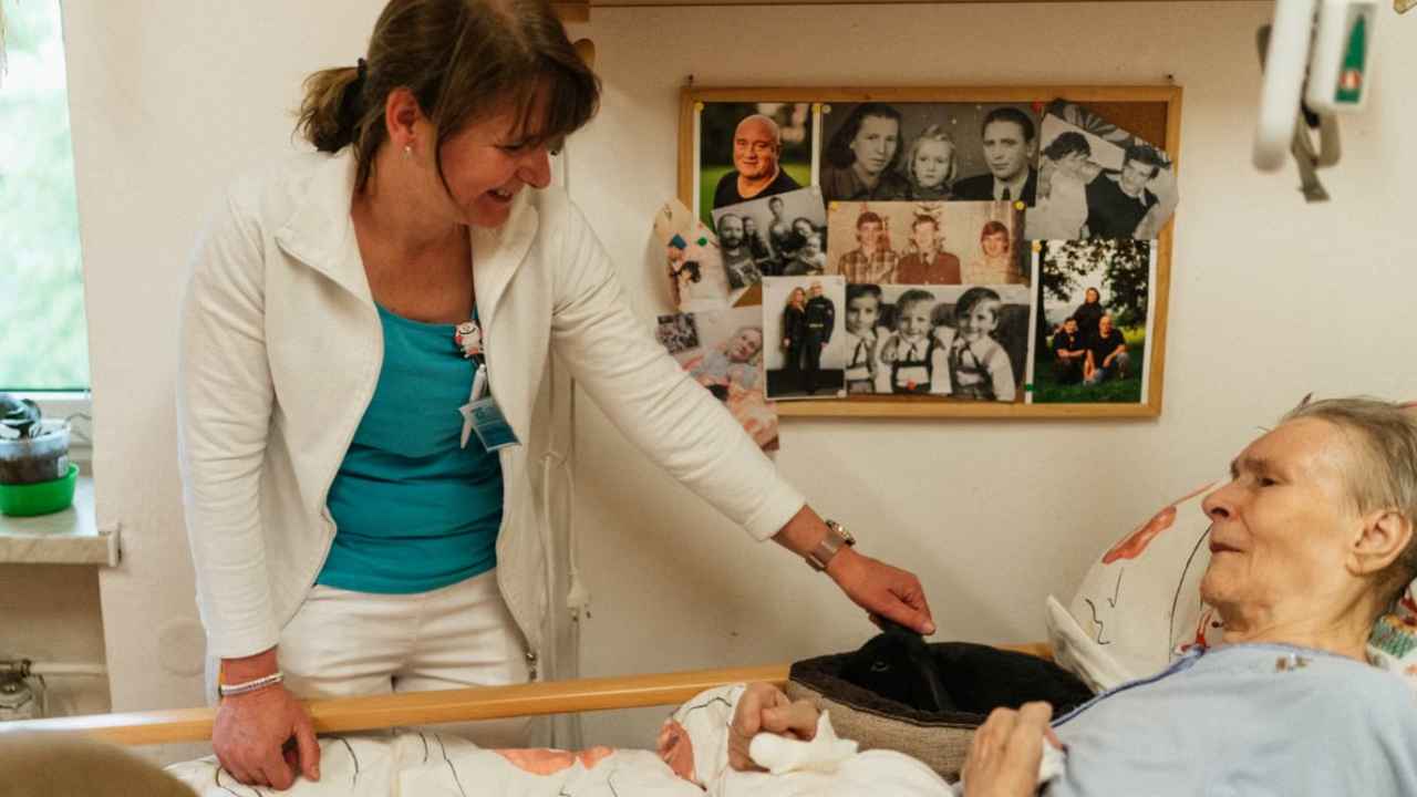 Una profesional atiende a una persona mayor en una cama.