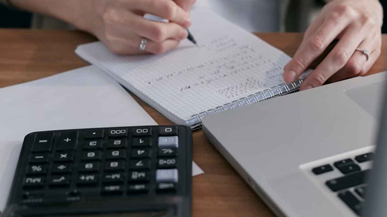Manos realizando cálculos junto a una calculadora y un portátil.