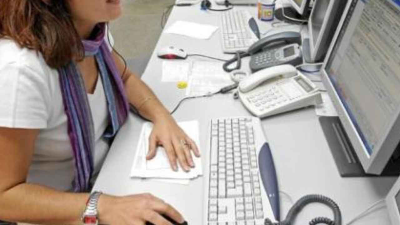 Teleoperadora trabajando con auriculares frente a varios ordenadores en un centro de atención telefónica