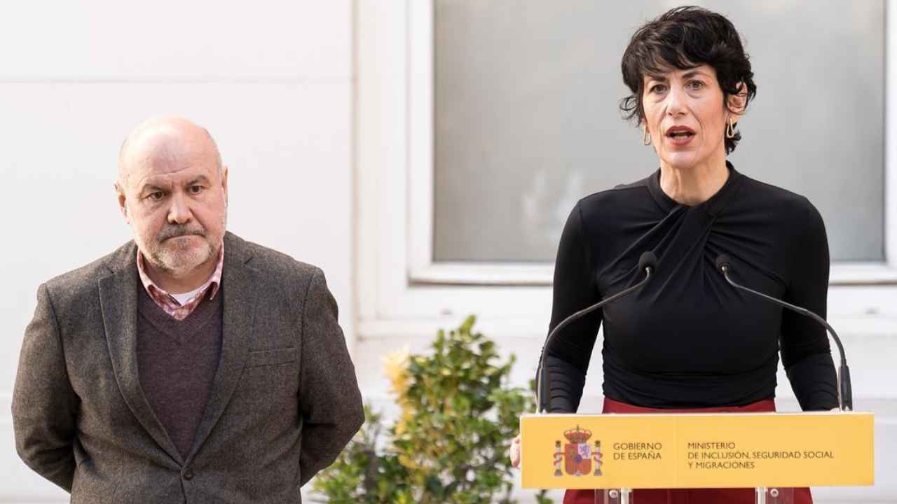 Elma Saiz interviniendo ante un atril del Ministerio de Inclusión, Seguridad Social y Migraciones, acompañada de un hombre.