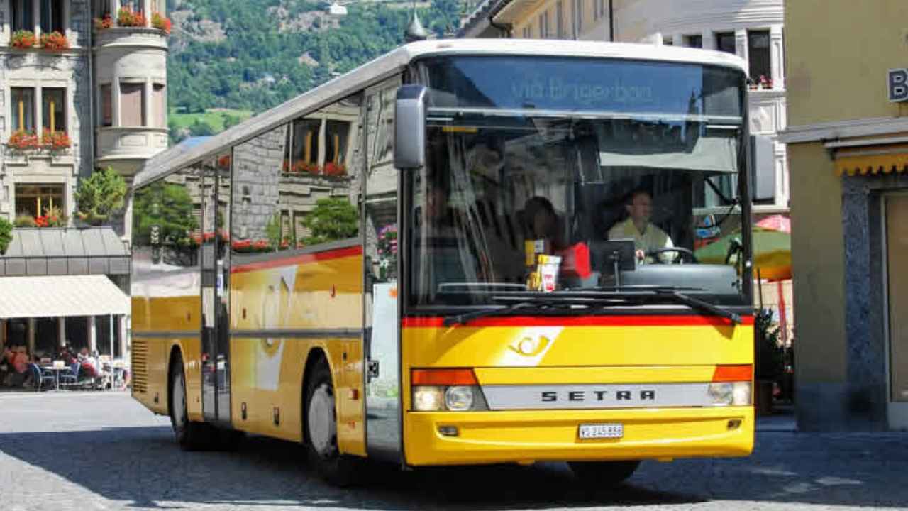 Autobús amarillo Setra en una plaza con edificios y montañas al fondo.