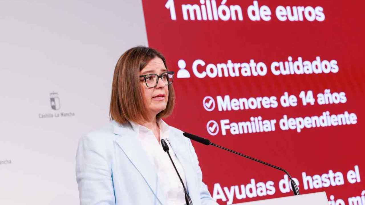 Mujer ante un atril junto a un panel sobre ayudas de conciliación en Castilla-La Mancha.