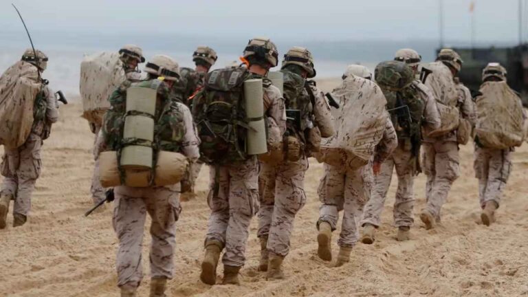 Soldados de las Fuerzas Armadas españolas caminando por una playa con uniforme militar y equipo de campaña.