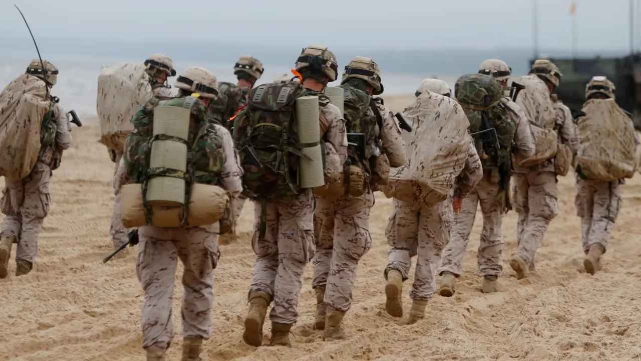 Soldados de las Fuerzas Armadas españolas caminando por una playa con uniforme militar y equipo de campaña.