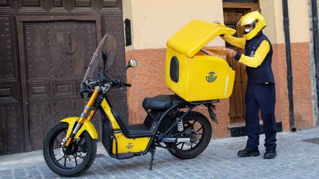 Cartero de Correos organizando cartas junto al compartimento abierto de una moto de reparto.