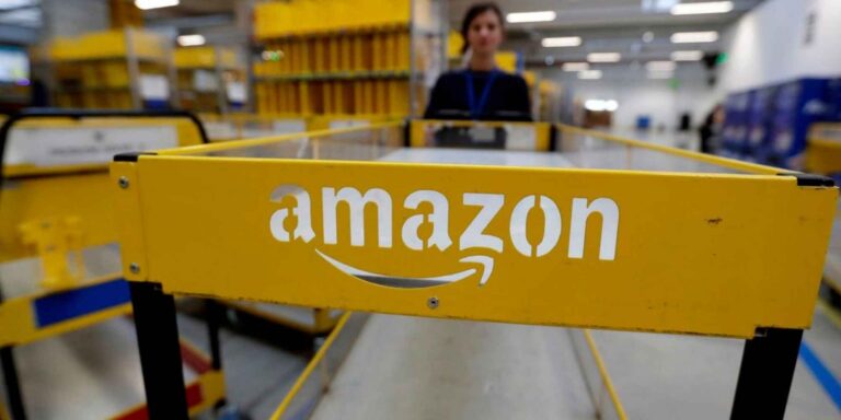 Cinta transportadora con el logotipo de Amazon en un centro logístico de la compañía, con una trabajadora al fondo. Copiar