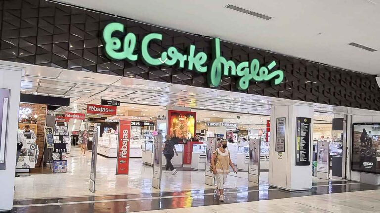 Entrada a un centro comercial de El Corte Inglés con el logotipo de la empresa y varios clientes en su interior.