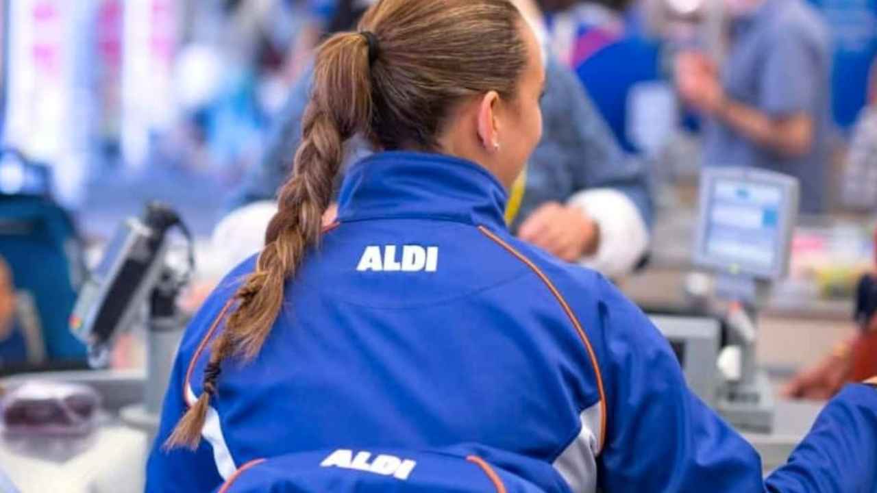 Trabajadora de ALDI con uniforme azul atendiendo a clientes en la zona de cajas de un supermercado.