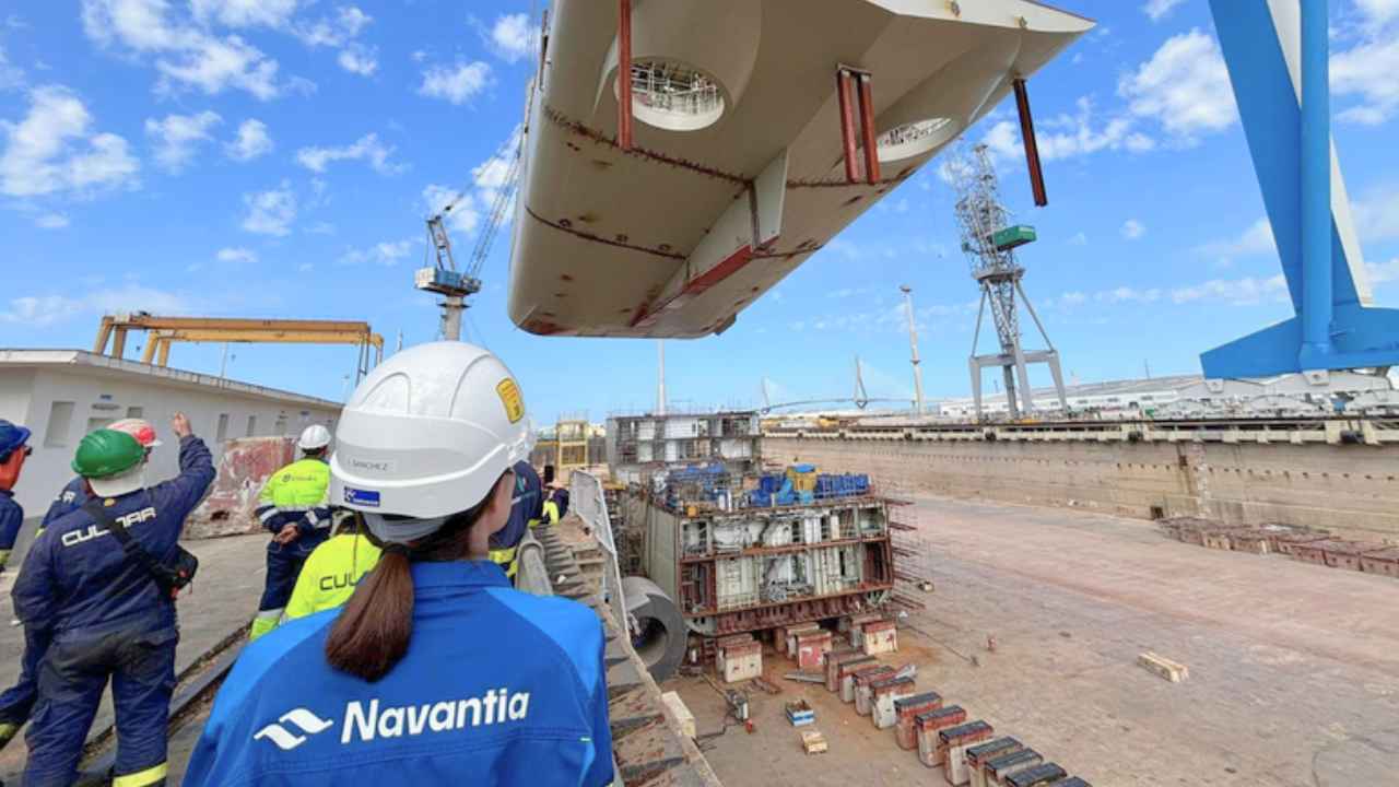 Personal de Navantia observa el izado de una estructura naval con una grúa en un astillero.