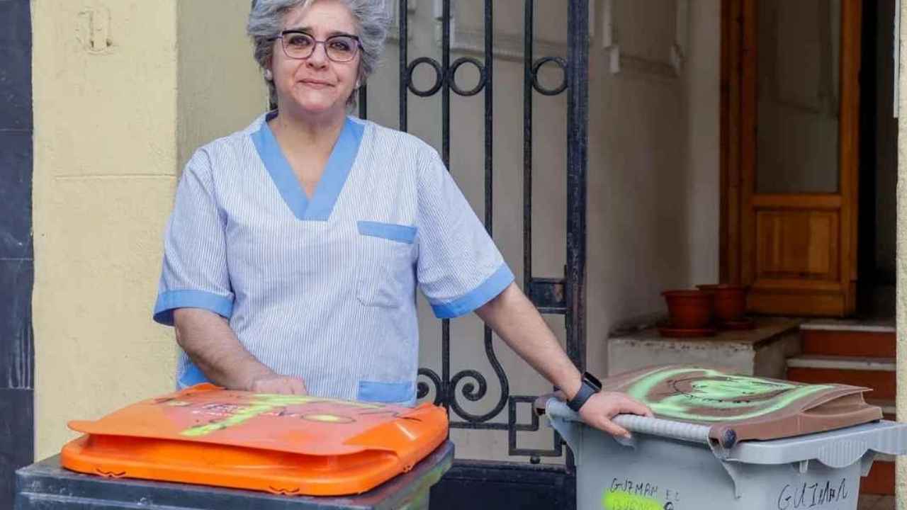 Infoemplea2 1 Trabajadora con uniforme azul junto a cubos de limpieza en la entrada de un edificio.