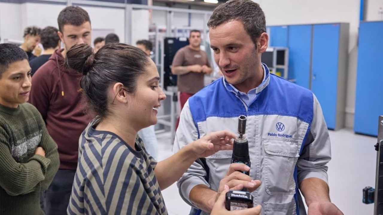 Alumna utiliza una herramienta eléctrica junto a un instructor de Volkswagen durante una formación en automoción.