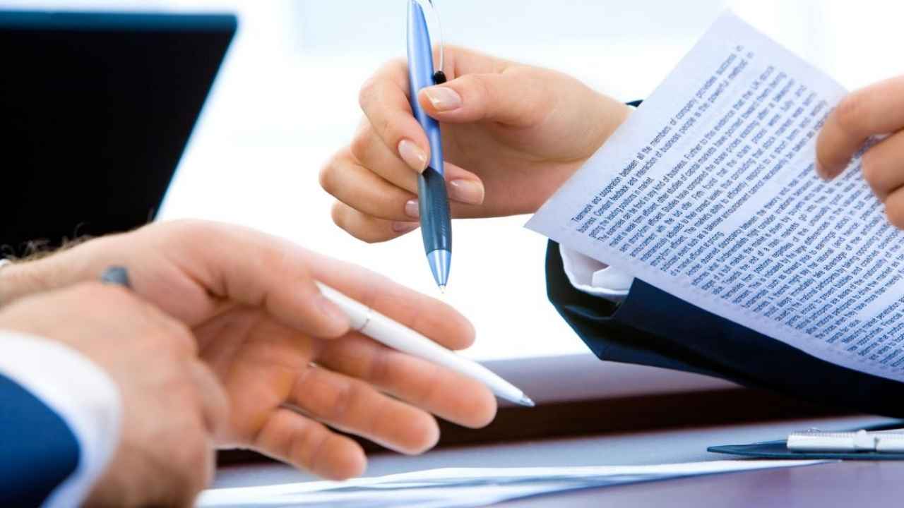 Manos de dos personas con bolígrafos revisando documentación sobre una mesa.