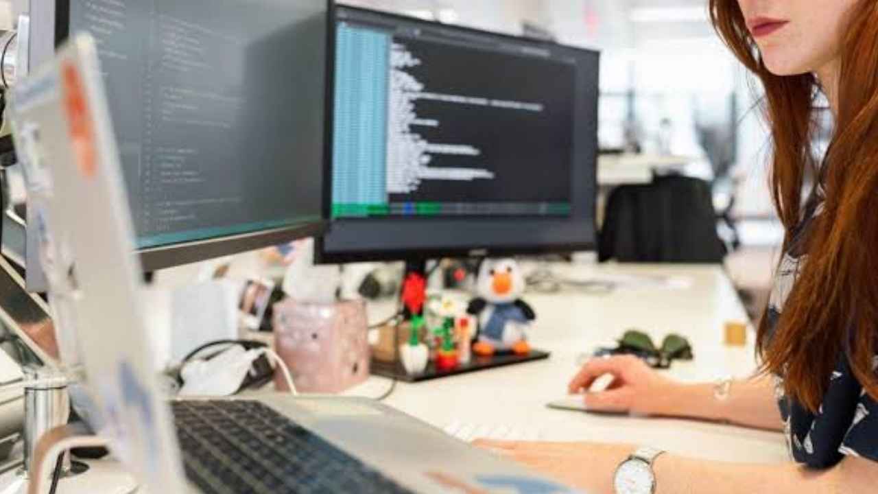 ALT Mujer trabajando con un ordenador portátil y dos monitores en una oficina.
