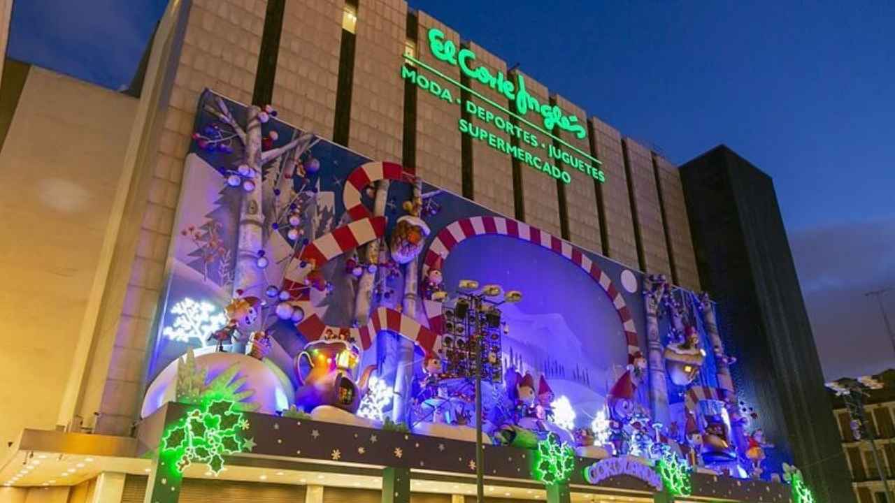 Fachada de El Corte Inglés con decoración navideña iluminada y personas junto a la entrada.