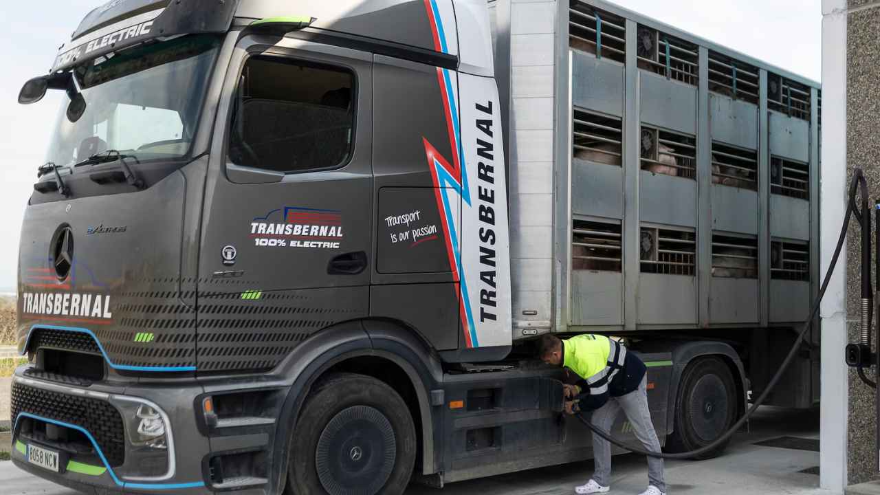 Trabajador conectando un camión eléctrico de transporte de mercancías a un punto de carga en unas instalaciones logísticas.