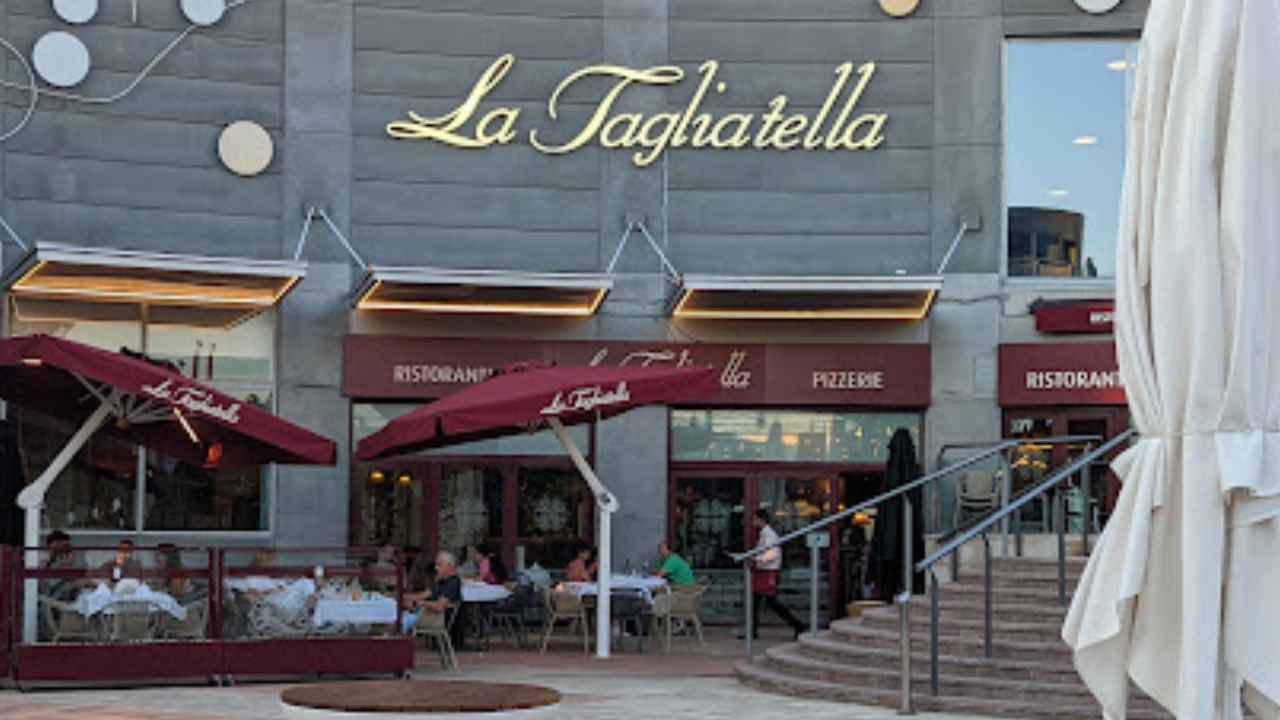 Fachada de un restaurante La Tagliatella con terraza exterior, mesas y clientes sentados en un centro comercial.