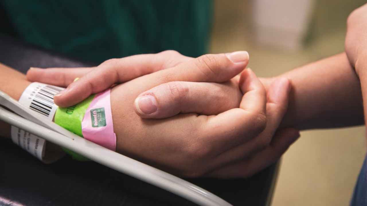 Primer plano de dos manos entrelazadas en un entorno sanitario.